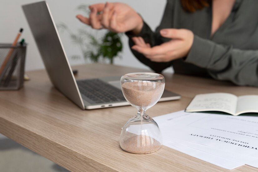 Woman in background working on laptop, with an hourglass tracking time in the foreground